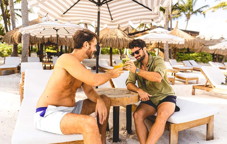Ana y Jose friends toasting, beach club, cocktails, striped umbrellas, beach vibe